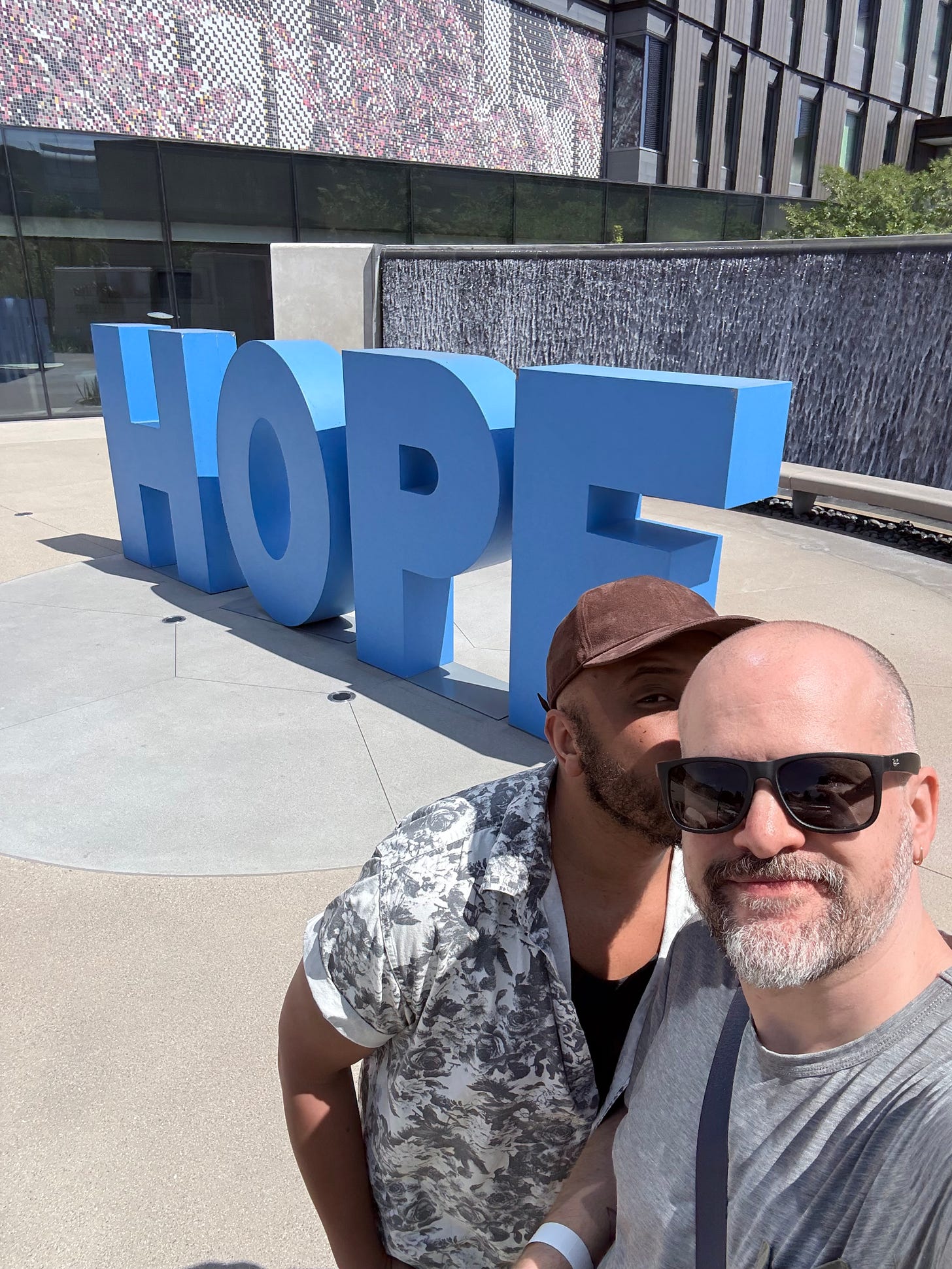 Rick and a friend hugging in front of the giant blue HOPE letters at City of Hope.